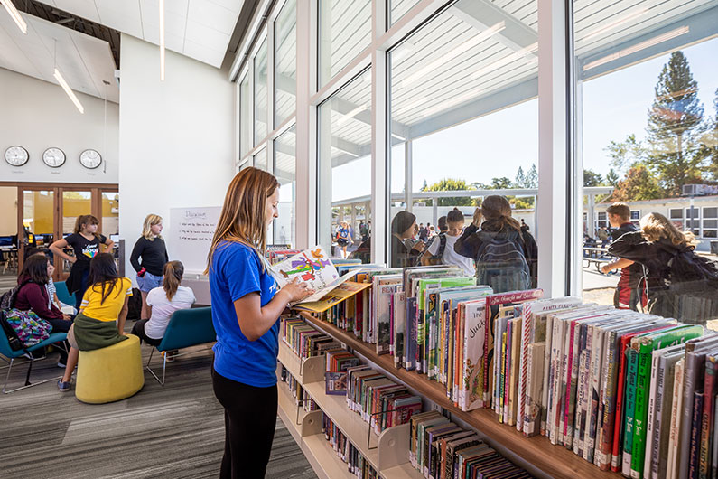 Several students browsing books inside Learning Resource Center with windows looking outside to Quad