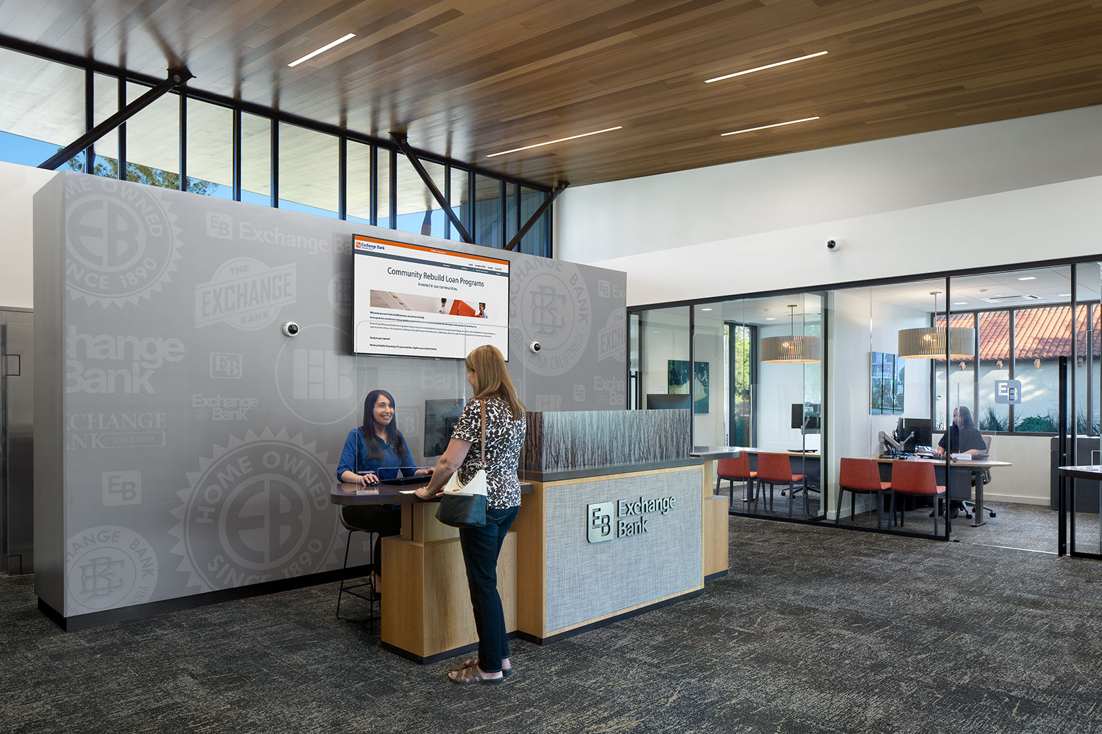 Teller helping customer with bank transaction and two offices in the background