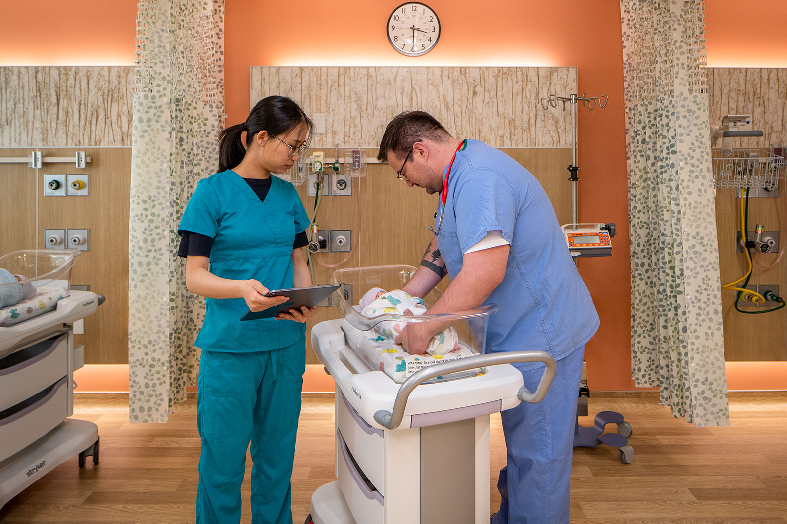 Nurse with chart observing second nurse handling infant