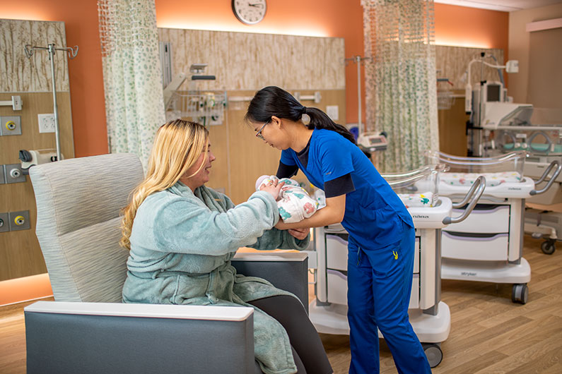 Nurse handing baby to mother in nursery setting