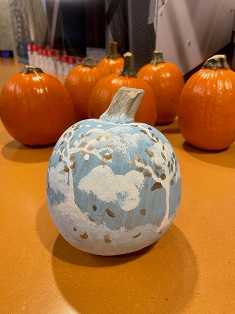 Blue, white and gold painted pumpkin with orange pumpkins in background