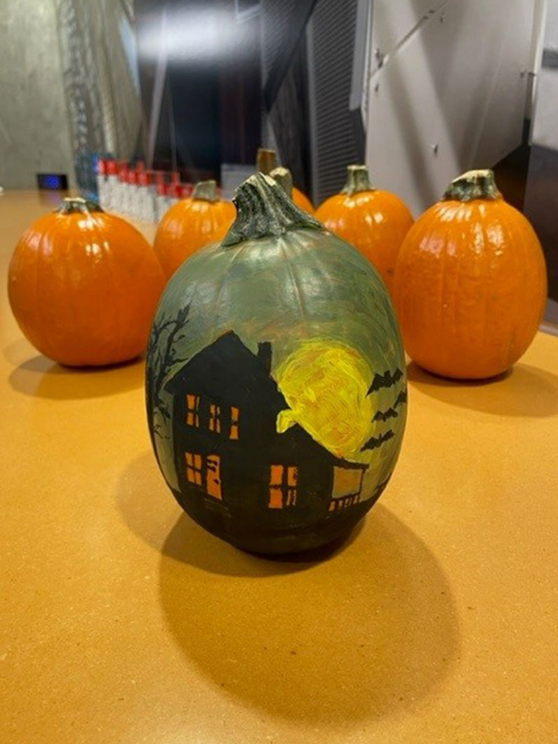 Haunted house painted on pumpkin with orange pumpkins in background