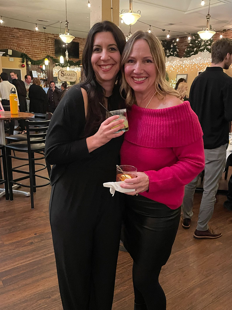 Two women with cocktails smiling at camera for TLCD's holiday party