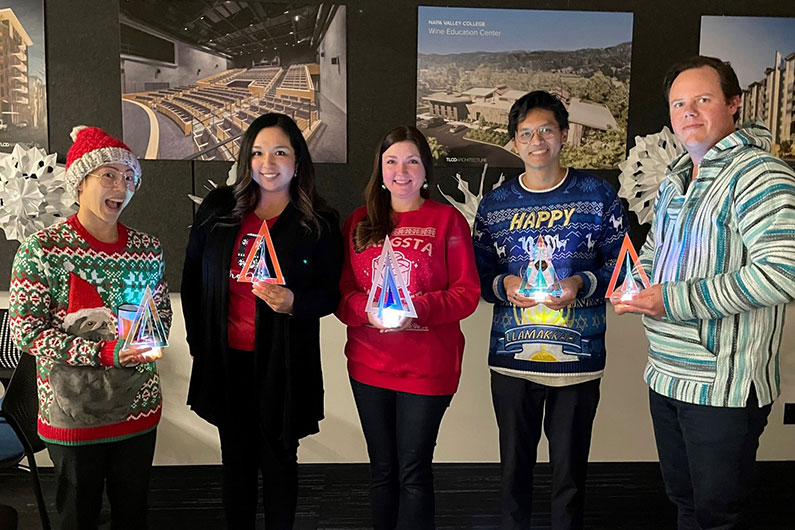 5 TLCD designers holding the acrylic holiday centerpieces while wearing holiday sweaters