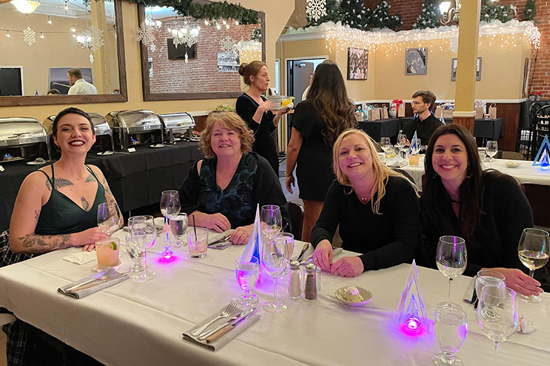 Several women sitting at table smiling at camera for TLCD holiday party