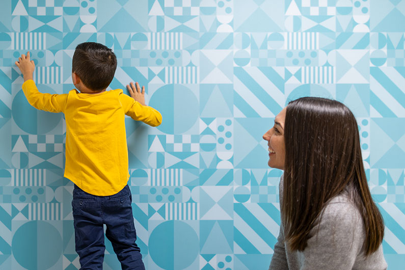 Mother and son in exam room with boy tracing geometric pattern on wall
