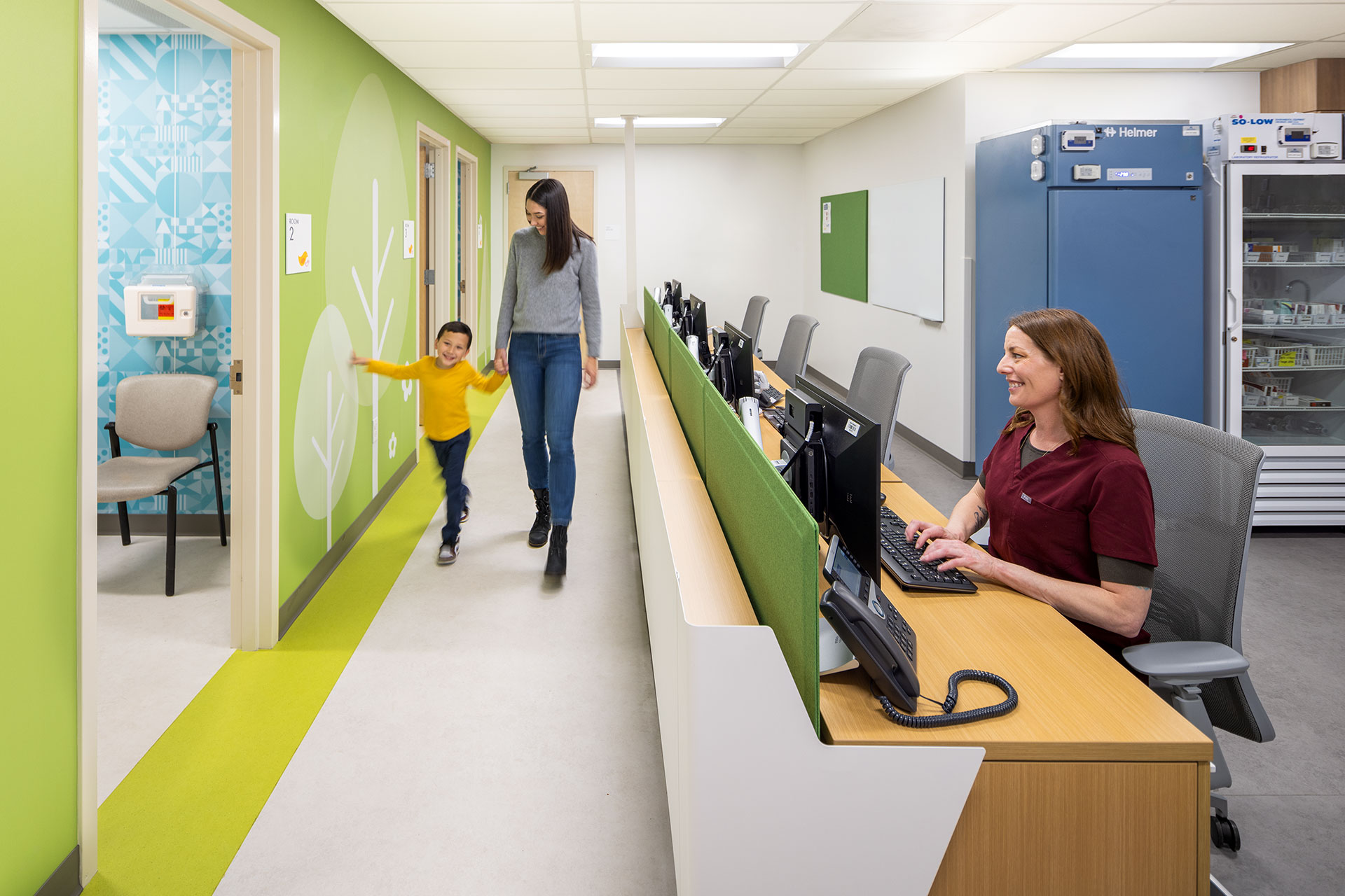 Healthcare design - Mother and son walking down a hall looking at wall mural with healthcare staff seated at desk