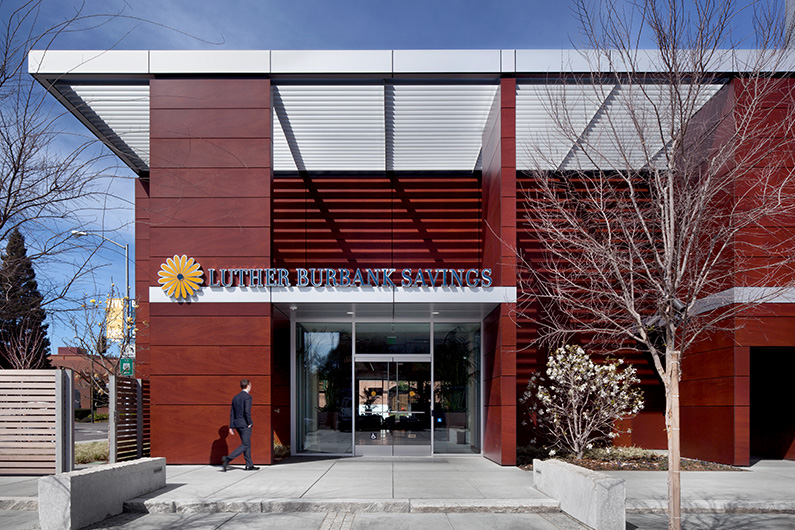 Entrance showing man walking into bank with contemporary exterior siding of wood and metal