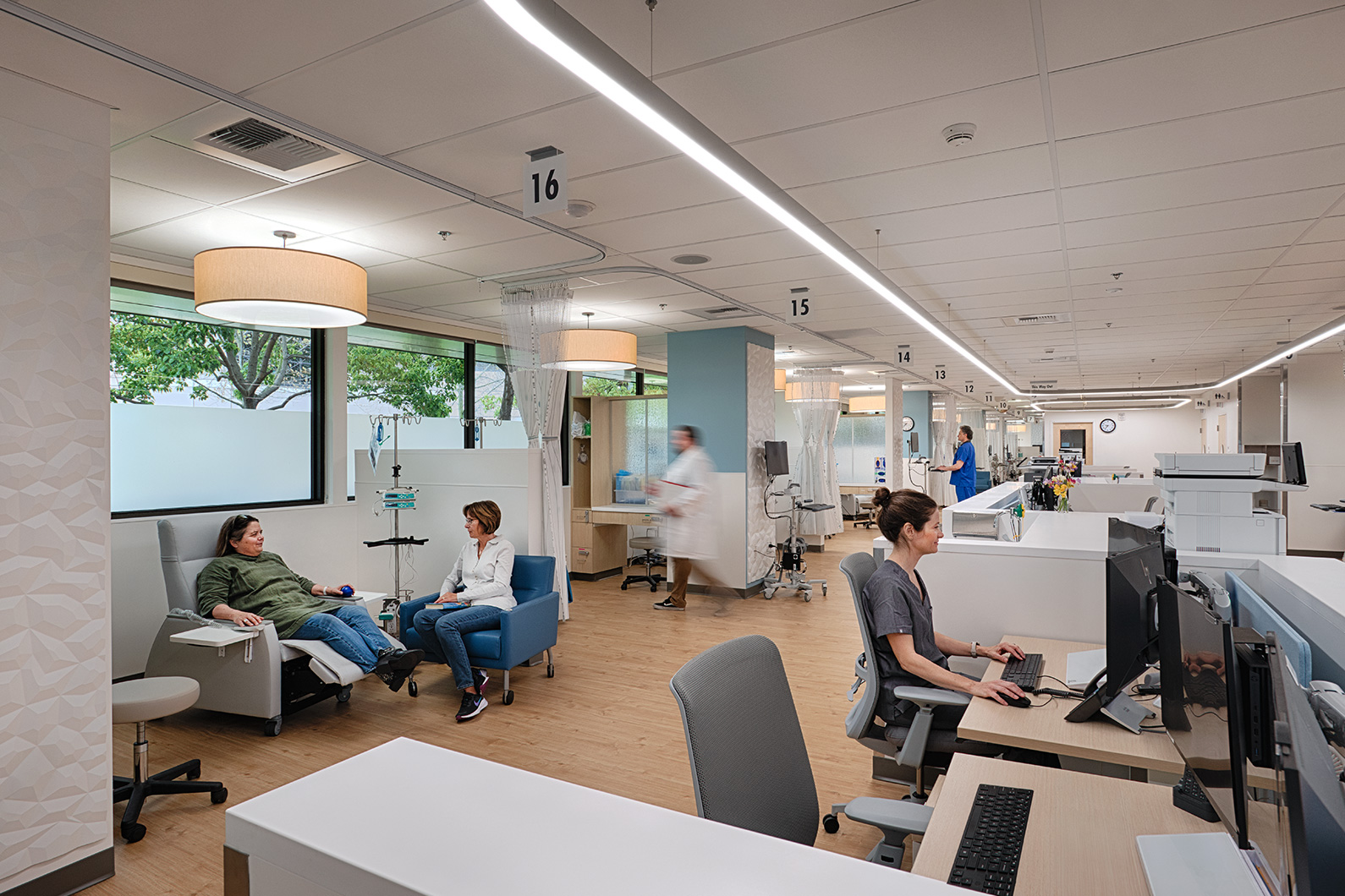 Healthcare design for critical care - Interior photo of patient and family member in Oncology infusion bay, with nursing staff in the background