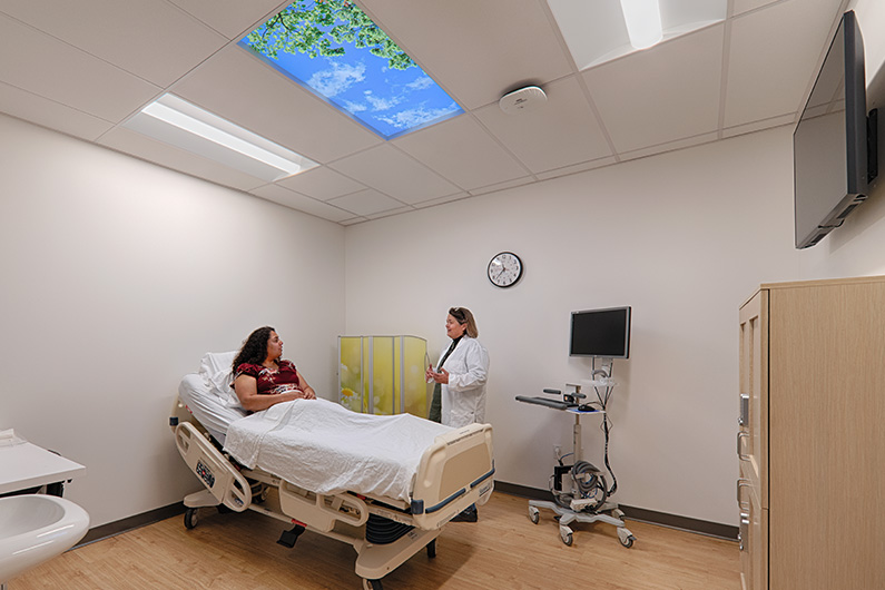 Interior photo of private treatment room with woman in bed talking to doctor