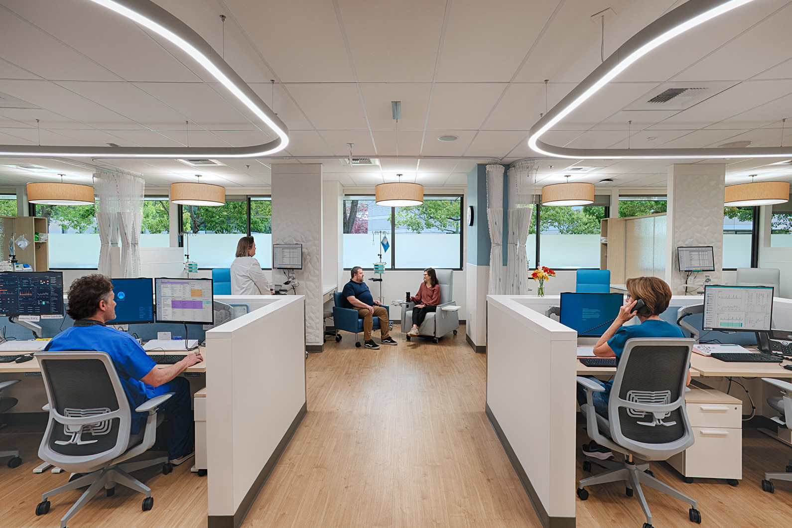 Two people sitting together in oncology infusion bay with a female nurse sitting to the right at desk, and male nurse sitting to the left at desk