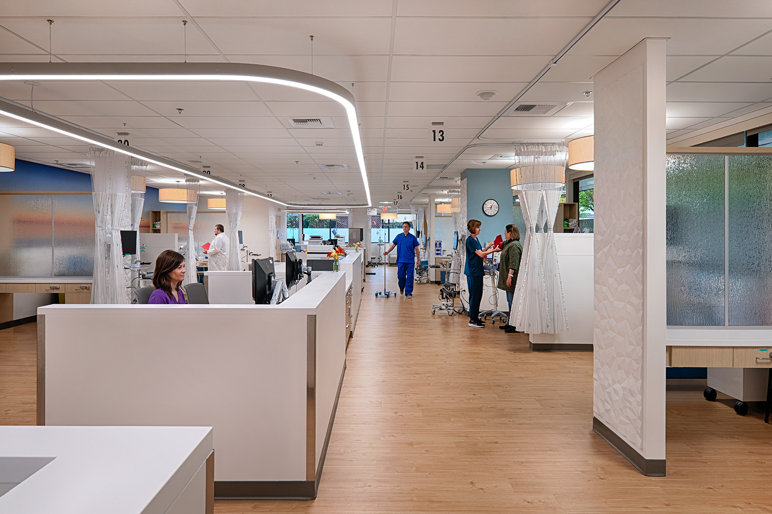 Interior photo looking down hallway at multiple oncology infusion bay with nurses stations across for observation