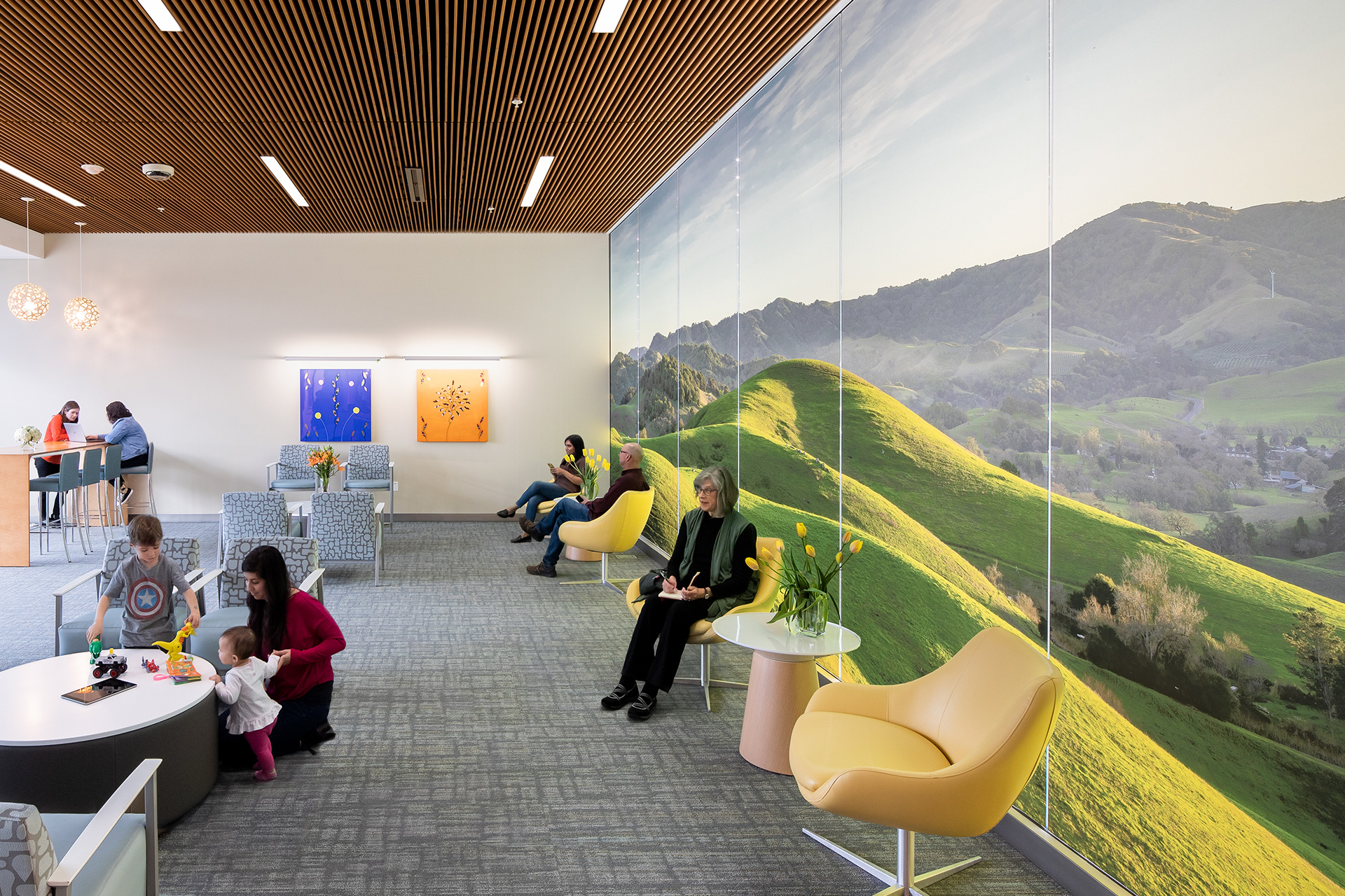 Several people sitting in waiting area at Kaiser Behavioral Health with warm colors, wall mural and residential furniture