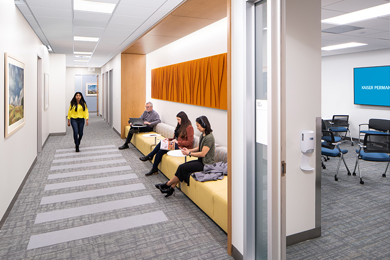 4 people waiting in a hallway lounge area with group therapy room in the background