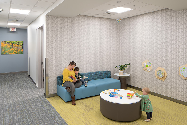 Mother and two children sitting in alcove with child scale toys and warm residential furniture