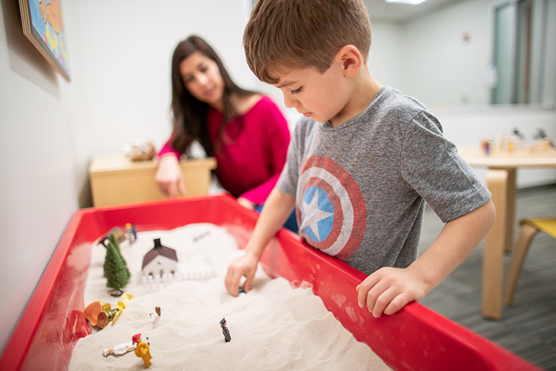 Female therapist with young boy playing with toys in sandbox in an observation room at Kaiser Behavioral Health