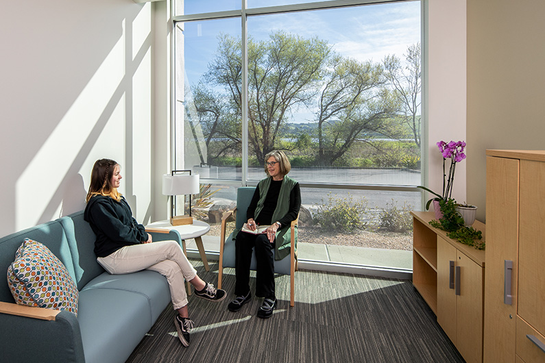 Female therapist talking to young woman in a private office with views to outdoor landscape