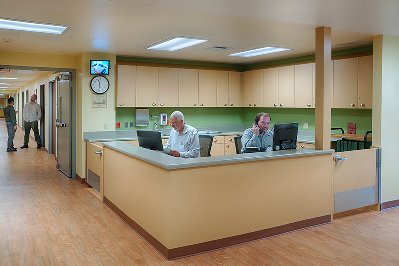 Two men seated and two men standing in hallway with views to patient rooms at Aurora Psychiatric Hospital