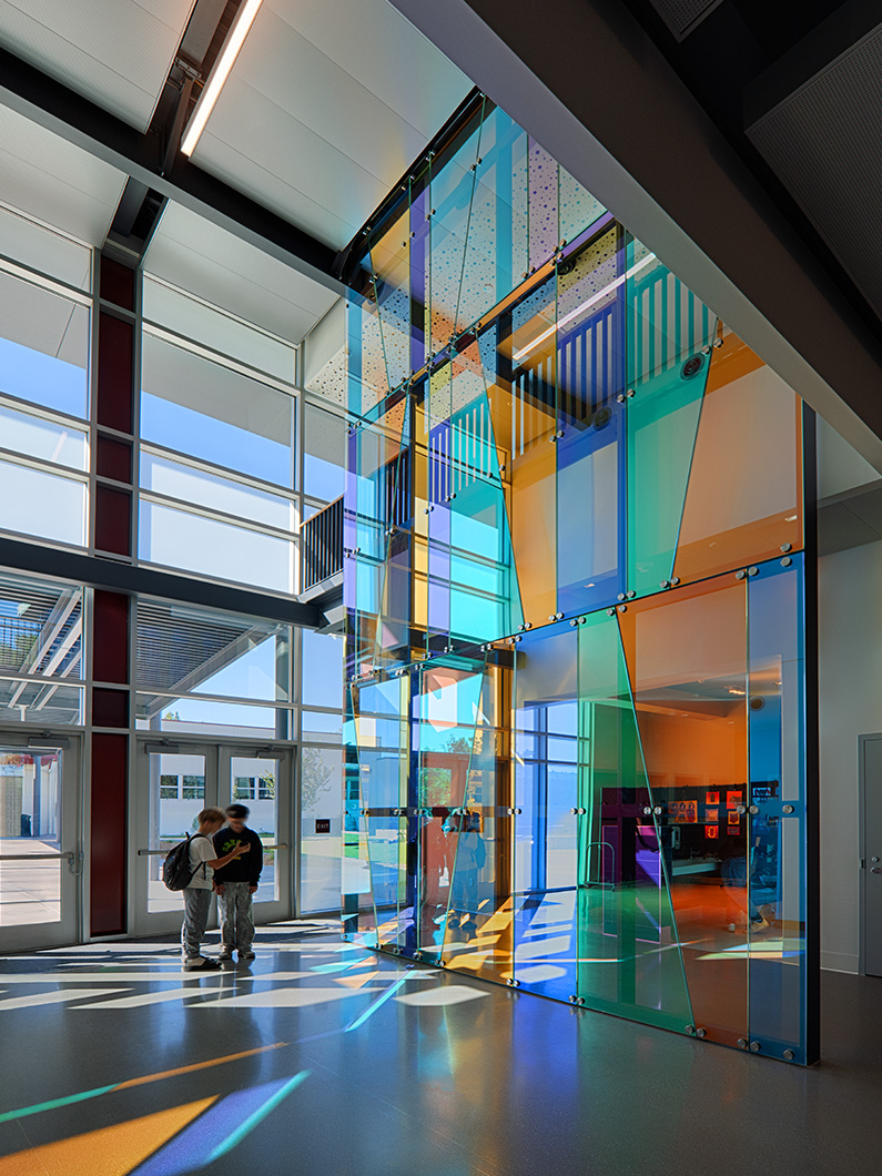 Interior photo of glass feature wall in lobby of classroom building with two students walking by
