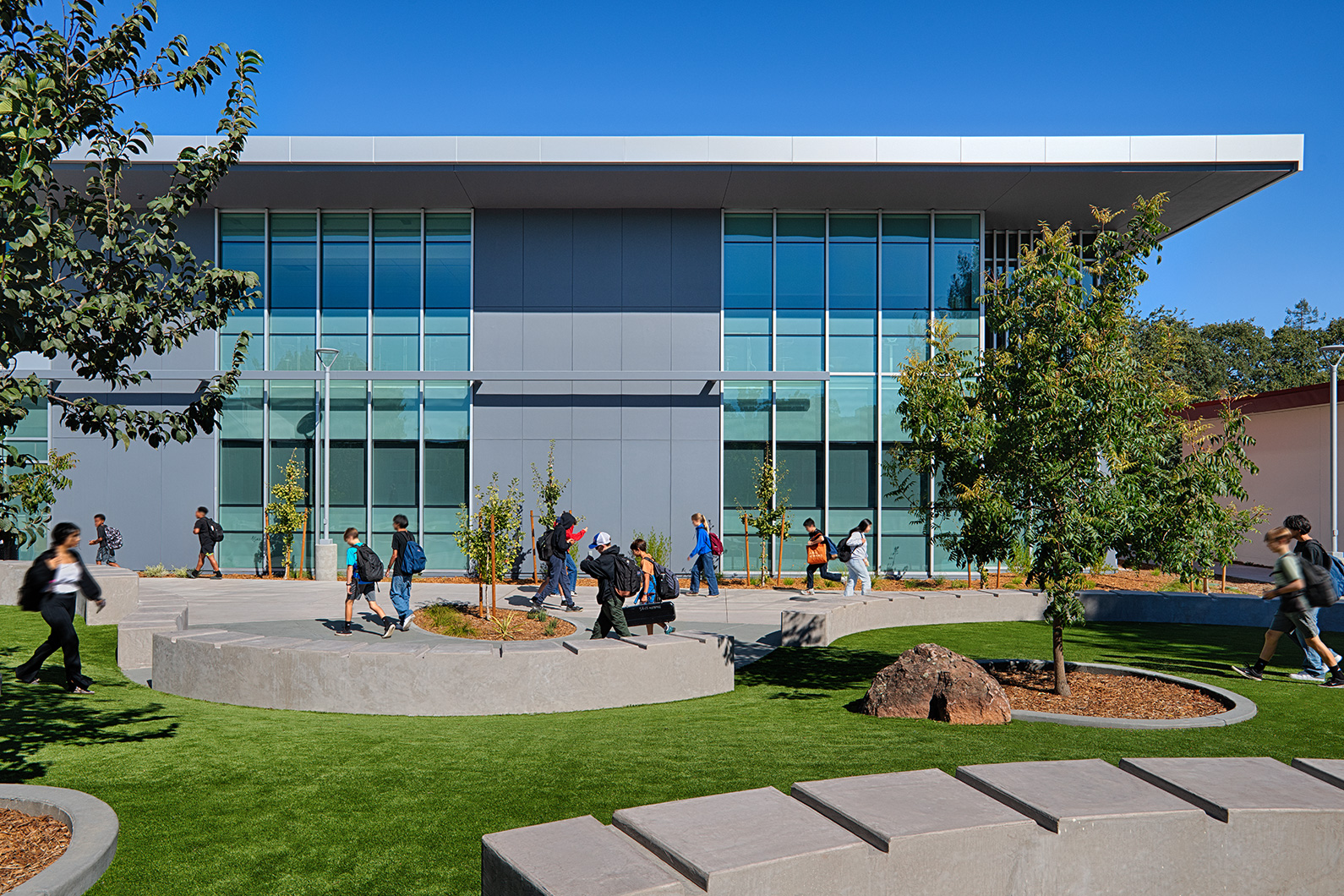 Exterior photo of classrooms building showing large expanse of glass for natural daylight, with courtyard in foreground